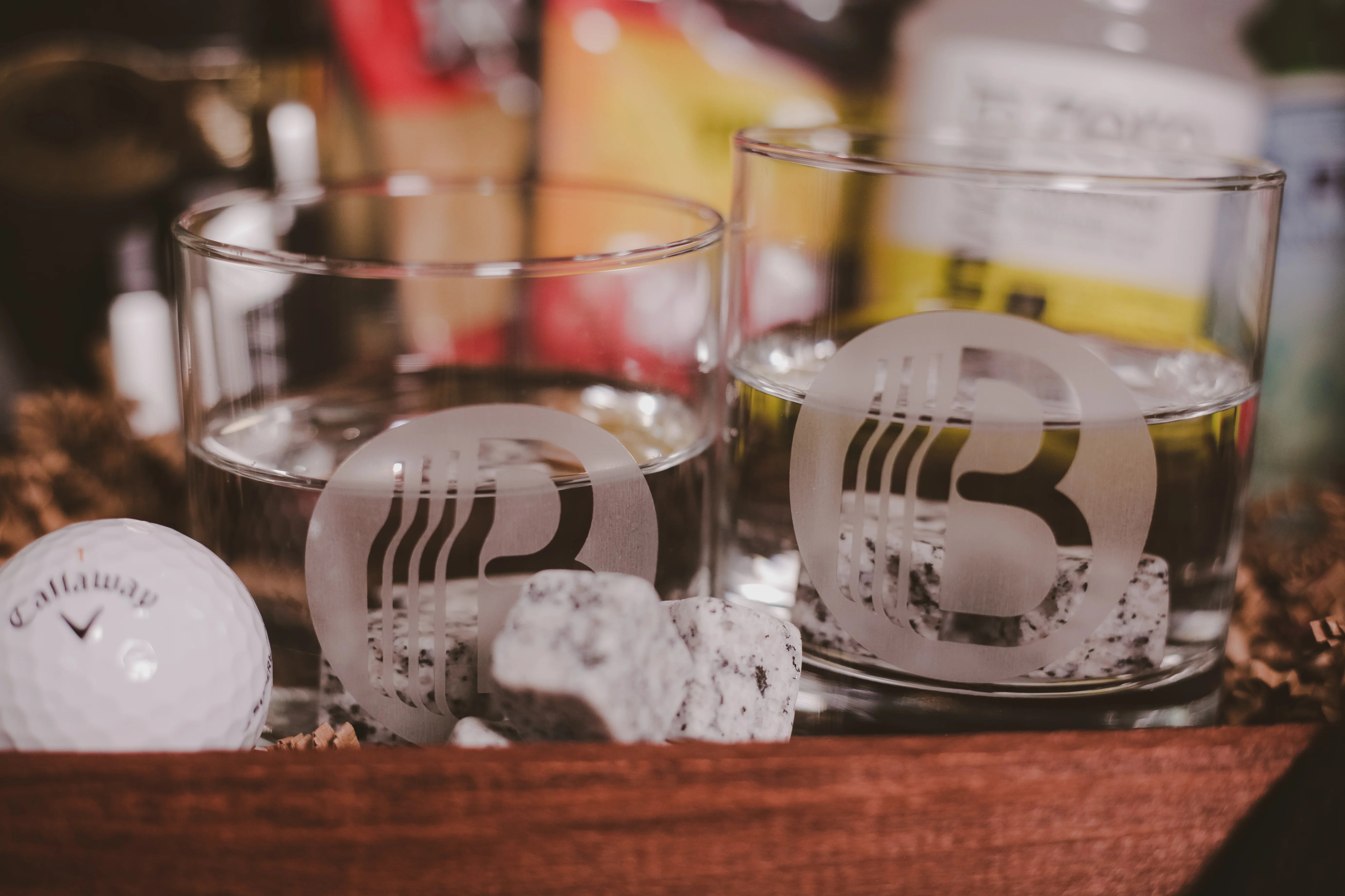 Gift basket from BroBasket including two whiskey glasses with etched logo, surrounded by whiskey stones and a Callaway golf ball in a wooden box setting.