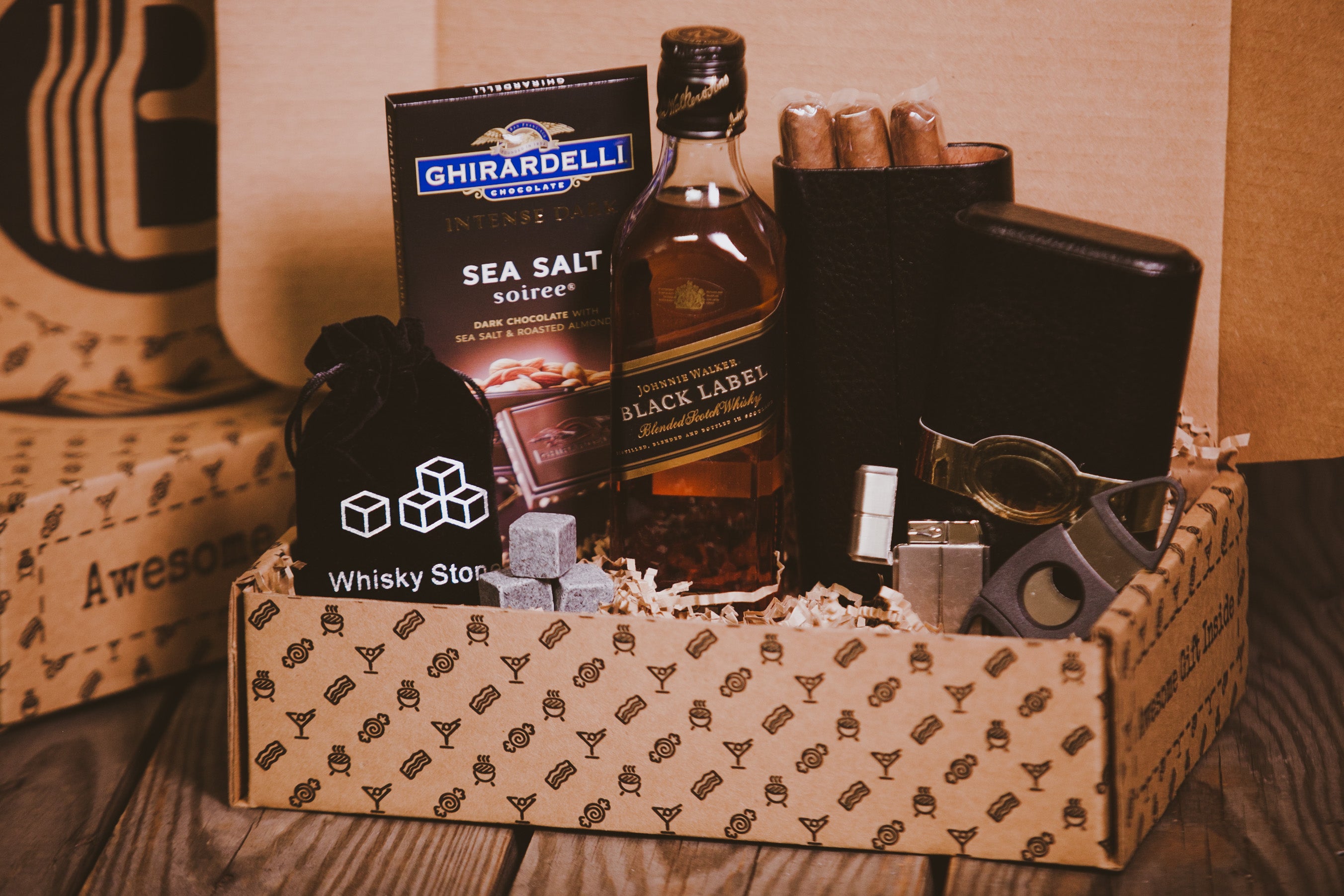 Gift basket from BroBasket with whiskey bottle, Ghirardelli sea salt chocolate, cigars, whisky stones, and accessories, presented in a decorative cardboard package.