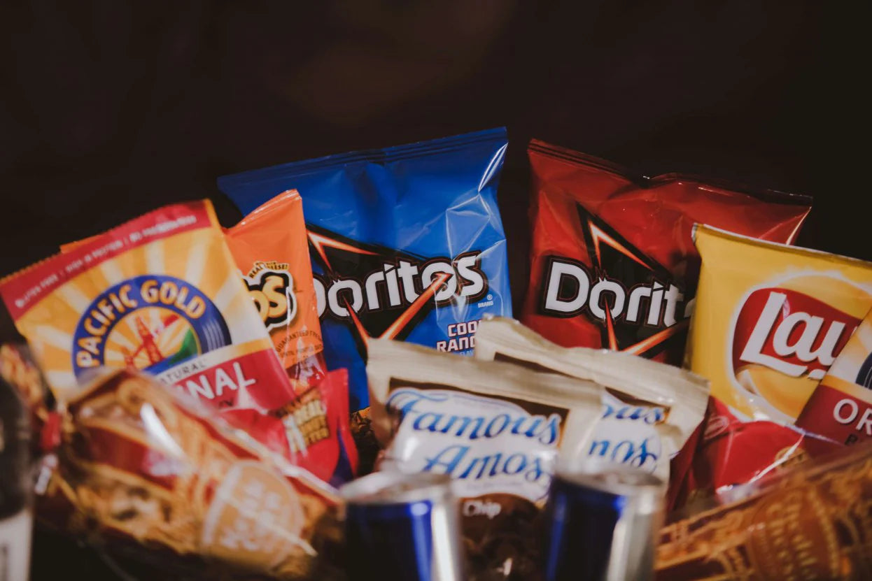 Assorted snack bags including Doritos, Lay's, Pacific Gold beef jerky, and Famous Amos cookies, arranged in a gift basket from BroBasket.