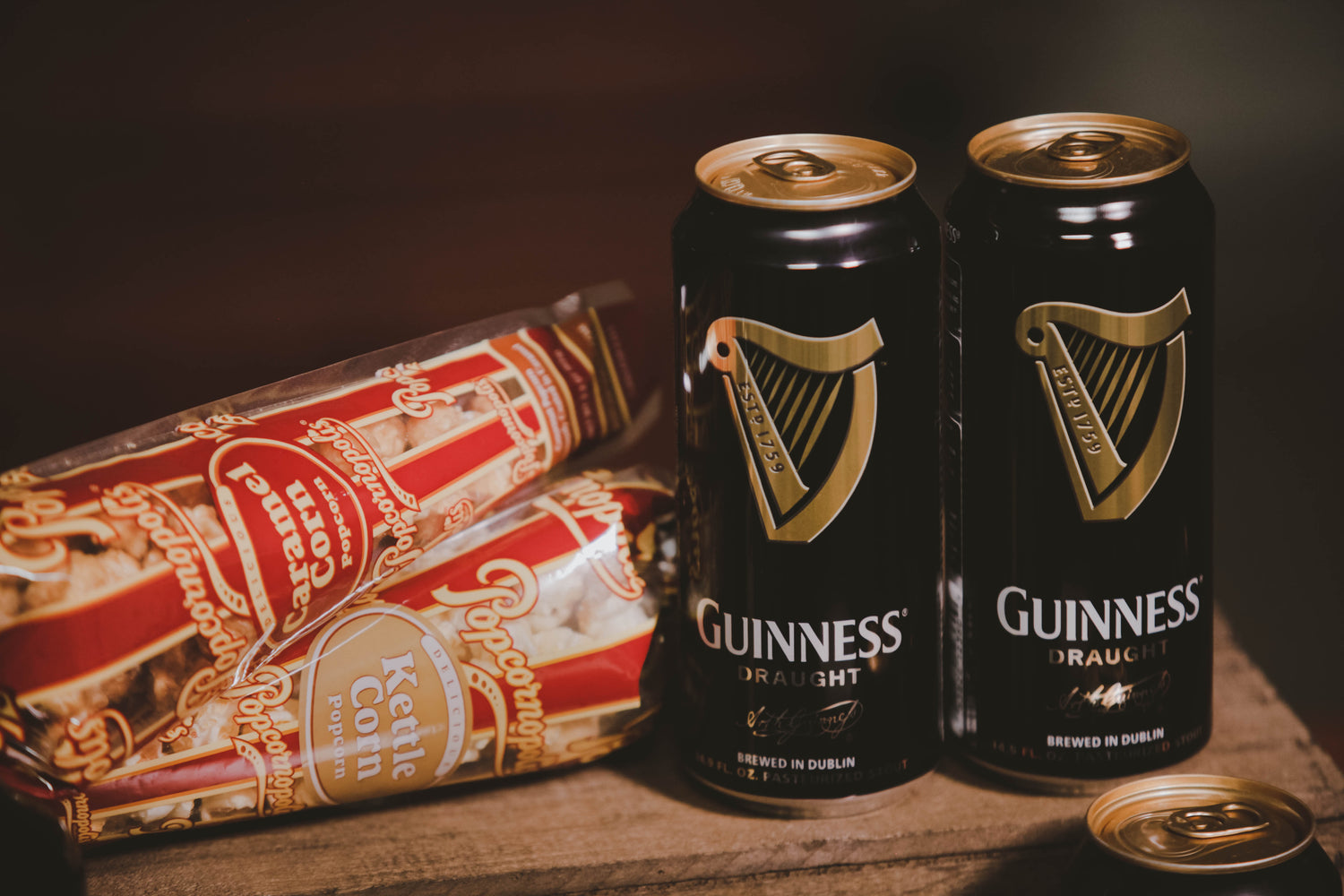 Gift basket from BroBasket including cans of Guinness Draught beer next to bags of caramel and kettle corn popcorn on a wooden surface.